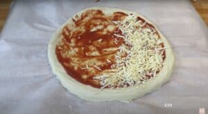 Half-topped pizza dough with tomato sauce and mozzarella on parchment paper, ready for baking.